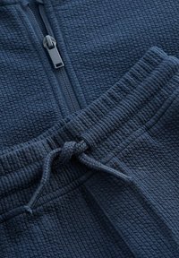 Mörkblå zip-up topp med våffelstruktur och framdragkedja samt matchande byxor med dragsko och ribbat midjeband och mudd.
