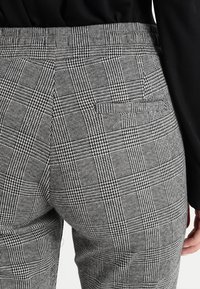 Pantalons à carreaux gris avec des lignes verticales et horizontales, présentant un tissu texturé et une taille ajustée.