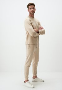 Beige sweatshirt and matching joggers made of soft fabric. Sweatshirt has a round neckline, joggers feature elastic cuffs. White sneakers.
