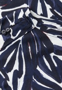 Mörkblå och vit mönstrad textil med svävande bladformer. Har en knappstängning, mjuk struktur och slät tygfinish.