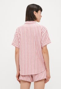 Chemise à manches courtes rayée rouge et blanche avec un col, assortie à un short. Le tissu a une apparence douce et texturée.