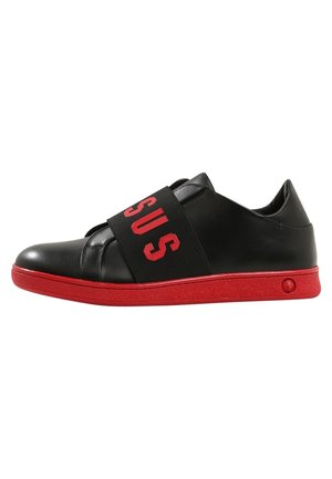 Baskets basses noires avec une large sangle noire comportant les lettres rouges "SUS" et une semelle ainsi qu’un liseré rouge vif.