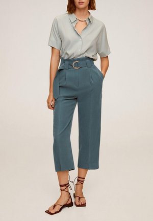 Chemise gris clair à manches courtes, pantalons teal taille haute avec une ceinture et une boucle circulaire, et sandales tan à lanières avec des semelles plates.