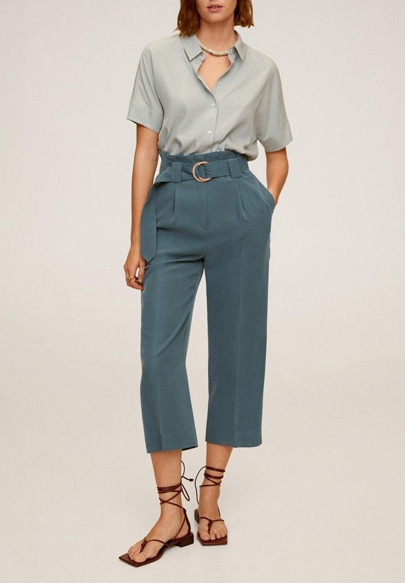 Chemise gris clair à manches courtes, pantalons teal taille haute avec une ceinture et une boucle circulaire, et sandales tan à lanières avec des semelles plates.