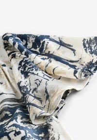 Tryckt tyg med en blandning av marinblå och beige färger, som visar abstrakta linjer och texturer, med en mjuk och flödande drape.