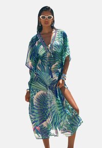 Sheer, multi-colored kaftan featuring a palm leaf print, V-neck, and side slits. Accented with beads and tassels on the front.