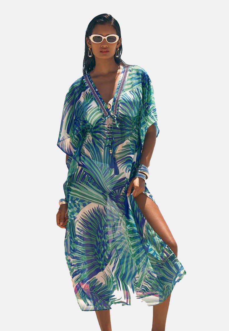 Sheer, multi-colored kaftan featuring a palm leaf print, V-neck, and side slits. Accented with beads and tassels on the front.
