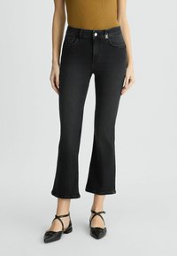 Jean flare noir en denim avec taille haute, poches avant et fermeture à boutons. Associé à des ballerines noires à lanières. Haut à côtes texturé.