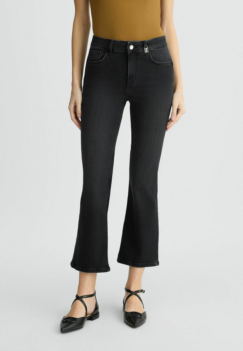 Jean flare noir en denim avec taille haute, poches avant et fermeture à boutons. Associé à des ballerines noires à lanières. Haut à côtes texturé.