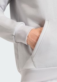 Ανοιχτό γκρίζο hoodie με υφή, που διαθέτει μπροστινή τσέπη και ριμπ μανσέτες. Το ύφασμα φαίνεται μαλακό και άνετο.