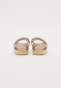 Beige Sandalen mit strukturierten Stoffriemen und metallischen Akzenten, ausgestattet mit einer geformten Sohle und einem offenen Rückendesign für einfaches Anziehen.