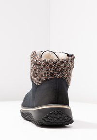 Botte noire à la cheville avec une tige en tricot texturé et à motifs et doublure en fausse fourrure. Comporte une semelle en caoutchouc avec un motif antidérapant et une bordure blanche contrastante.
