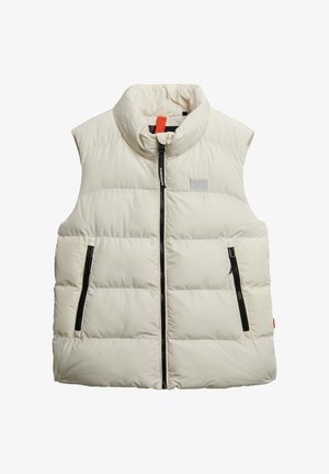 Chaleco acolchado crema con cuello alto, cremallera frontal de doble sentido y dos bolsillos laterales con cremallera. Presenta un parche de logo en el pecho y una textura suave.