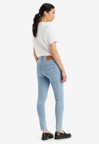 Vaqueros skinny azul claro con dobladillo deshilachado, de tiro medio, y parche de cuero en la parte posterior; combinados con una camisa blanca de manga corta y calzado negro.