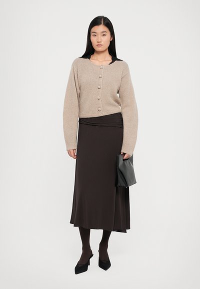 Beige knitted cardigan with large buttons, paired with a brown fitted skirt, black tights, and pointed black heels. Carrying a black clutch.