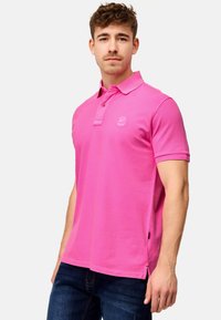Slankekropp polo skjorte i knallrosa, med to-knapp placket, korte ermer og sidesplitter for bevegelsesfrihet. Teksturert bomullsstoff.