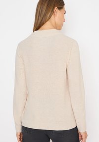 Beige leichter Pullover mit geripptem Design, langen Ärmeln und Rundhalsausschnitt, der eine glatte, weiche Oberfläche zeigt.