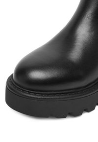 Czarny skórzany botek za kostkę z okrągłym noskiem, grubą podeszwą z trakcją i widocznym przeszyciem wzdłuż krawędzi. Gładka faktura na całej powierzchni.