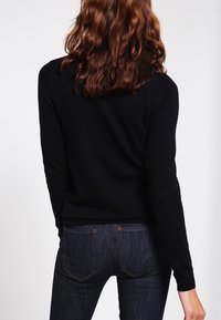 Svart stickad tröja med lång ärm, figurnära design, ribbade manschetter, kombinerad med mörkblå jeans med bakfickor och diskret sömnad.