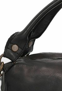 Zwart leren handtasdetail met de focus op het gestructureerde oppervlak, de gebogen handgreep, metalen hardware en contrasterende stiksels.