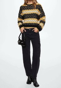 Maglione a maglia chunky con strisce orizzontali nere, gialle e bianche; pantaloni cargo neri; piccola borsa nera; stivaletti neri.