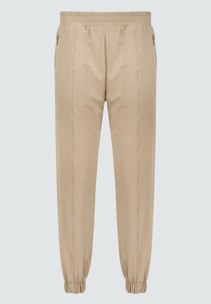 Pantalons de jogging beige avec une taille élastique, des poches zippées et des poignets élastiques aux chevilles. Texture du tissu lisse avec un design soigné.