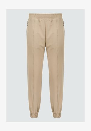 Pantalons de jogging beige avec une taille élastique, des poches zippées et des poignets élastiques aux chevilles. Texture du tissu lisse avec un design soigné.