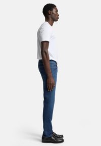 Slim-fit blå jeans med mellomvask, med fem lommer og klassisk design. Kombinert med en tettsittende hvit t-skjorte og svarte sko.