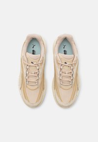 Beige sneakers with a textured mesh upper, cream accents, and yellow detailing. Features round laces, padded tongue, and cushioned sole.