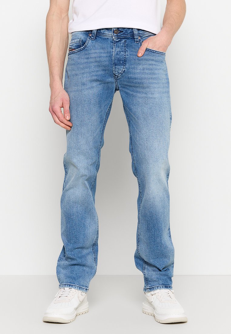 Jean en denim bleu clair avec une coupe droite, design à cinq poches et surpiqûres contrastantes. Porté avec des baskets blanches.