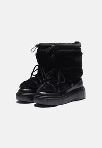Zwarte enkelboots met een combinatie van pluche en gladde texturen, voorzien van een dikke zool, verstelbare veters en een omgeslagen manchetontwerp.