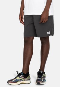 Gray shorts with a relaxed fit and side pockets. Features a small logo patch on the lower hem. Worn with multicolored athletic shoes.