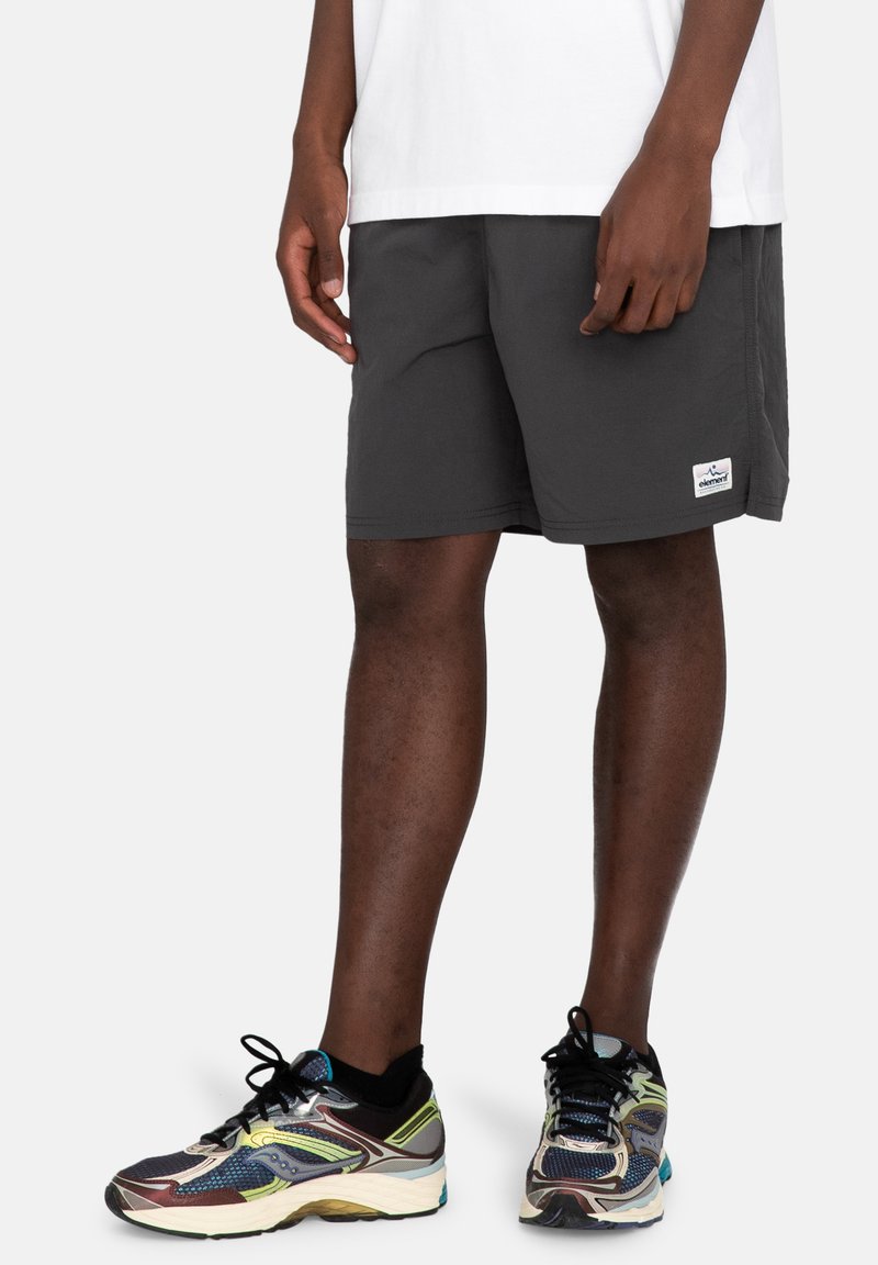 Gray shorts with a relaxed fit and side pockets. Features a small logo patch on the lower hem. Worn with multicolored athletic shoes.