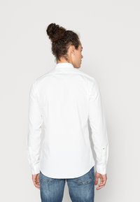 Witte lange mouwen overhemd met een puntige kraag, rugplooien en verstelbare manchetten, gedragen met blauwe jeans. Gladde textuur, tailored fit.