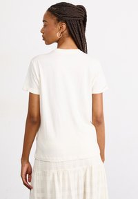 Korte mouwen crème t-shirt van zachte katoen, met een klassieke ronde hals en een ontspannen pasvorm, gecombineerd met een lichte, gestructureerde rok.