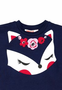 Granatowa koszulka z nadrukiem z kreskówkową twarzą lisa z kwiecistą koroną, białymi i czerwonymi akcentami oraz zamkniętymi oczami. Gładka bawełniana tekstura.