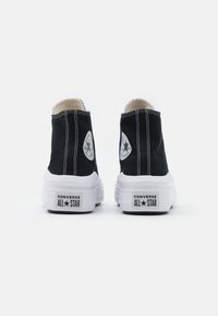 Baskets montantes en toile noire avec semelle blanche, ornées du patch logo Converse All Star sur les deux côtés et d'un détail de couture contrastante.