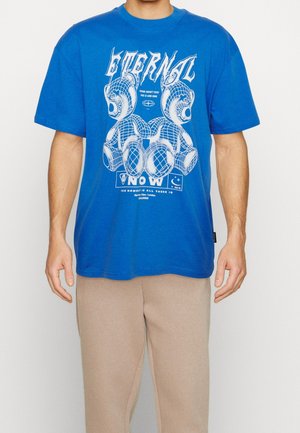 Niebieska bawełniana koszulka z graficznym nadrukiem, na którym znajdują się białe napisy i wzory niedźwiedzi. Koszulka ma luźny krój i okrągły dekolt.