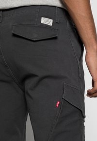 Närbild av svarta Levi's-byxor som visar bak- och sidofickor med synlig röd Levi's-tag och varumärkesetikett på midjan.