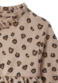 Beiges Kleid mit Rüschensaum, das ein Muster aus dunkel- und hellbraunen herzförmigen Flecken aufweist, hergestellt aus einem weichen, strukturierten Stoff.