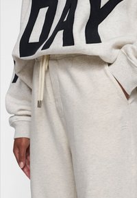 Sudadera gris claro con letras negras, con un ajuste relajado, puños de canalé y cordón con puntas de metal. Tejido suave y texturizado.