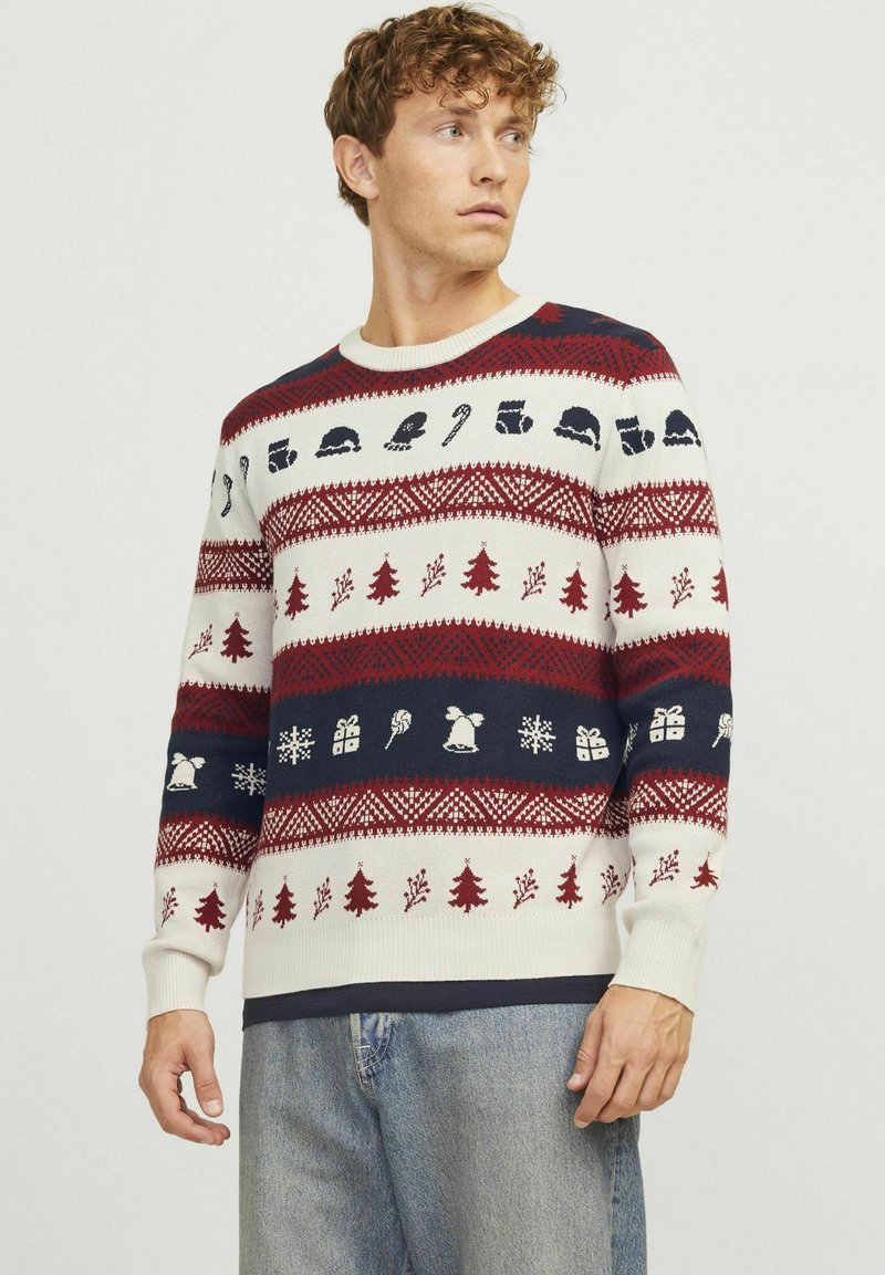 Pull de Noël tricoté arborant des couleurs rouge, marine et crème, avec des motifs d'arbres, de cadeaux et d'icônes saisonnières dans un design à rayures horizontales.