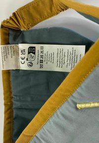 Unutrašnjost od plavog materijala sa žutim obrubom, s oznakom za njegu koja sadrži upute i simbole za održavanje. Glatka tekstura, pravokutnog oblika.