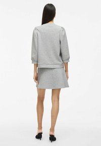 Sweatshirt gris avec un col rond et des manches bouffantes, associé à une jupe gris évasée, portée avec des sandales à talons ouverts noires.