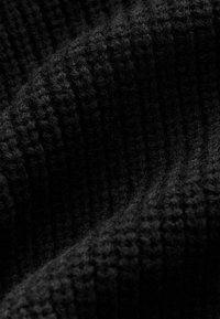 Sort strikket stof med en ribbet tekstur og bløde, fuzzy fibre. Materialet ser tykt og varmt ud og viser subtile variationer i nuanceringen.