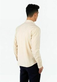 Beige långärmad skjorta med krage, bakveck och rundad nederkant. Texturerat tyg med knappdetaljer på ärmsluten.