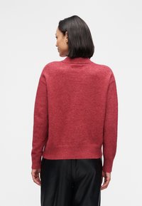 Pull rouge texturé à col montant et manches longues. Ourlet et poignets côtelés, en matière tricotée douce, présenté de dos.