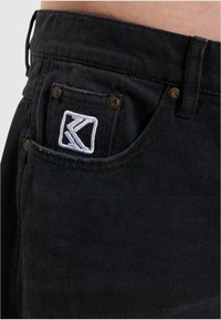 Los pantalones vaqueros de mezclilla negra presentan un acabado texturizado, un logo bordado en el bolsillo trasero y remaches de cobre que acentúan el diseño.