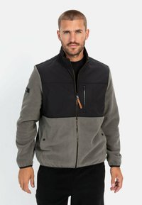 Fleecejacke mit schwarzem Oberteil und grauem Unterteil, ausgestattet mit einer Reißverschlusstasche auf der Brust, Reißverschluss und verstellbaren Bündchen.
