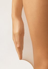 Průhledné béžové punčochy držící na stehně, zobrazující hladkou, lehkou texturu a mírně lesklý povrch, s bezproblémovým designem.